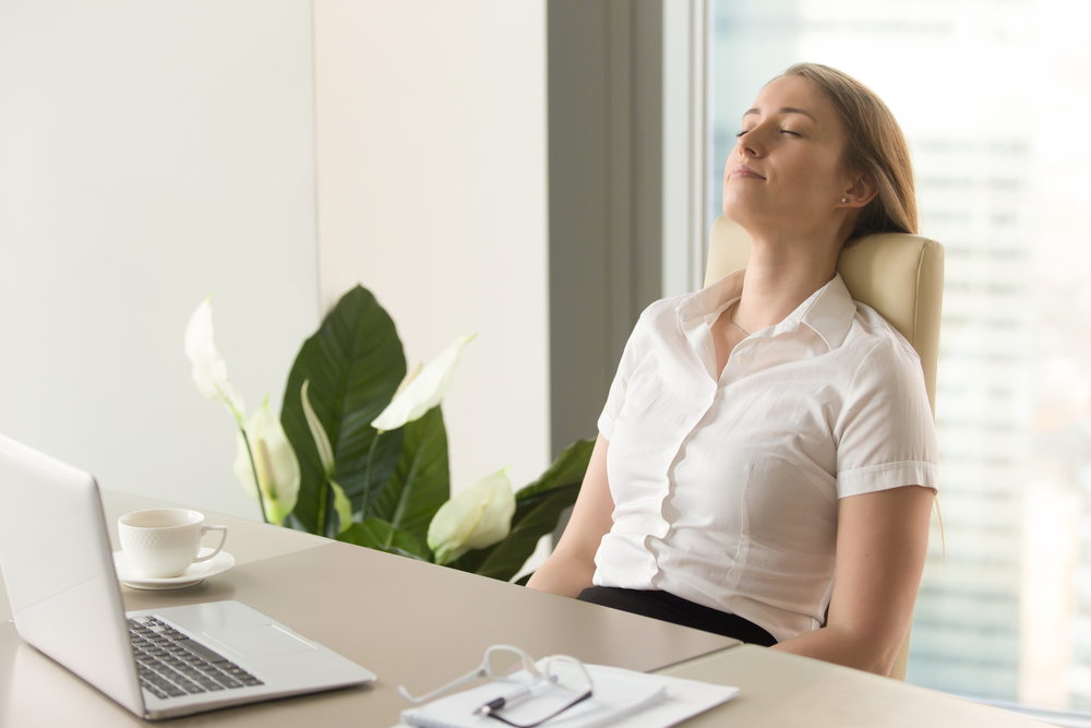 A woman meditating at her desk; mindfulness meditation can increase productivity at work.